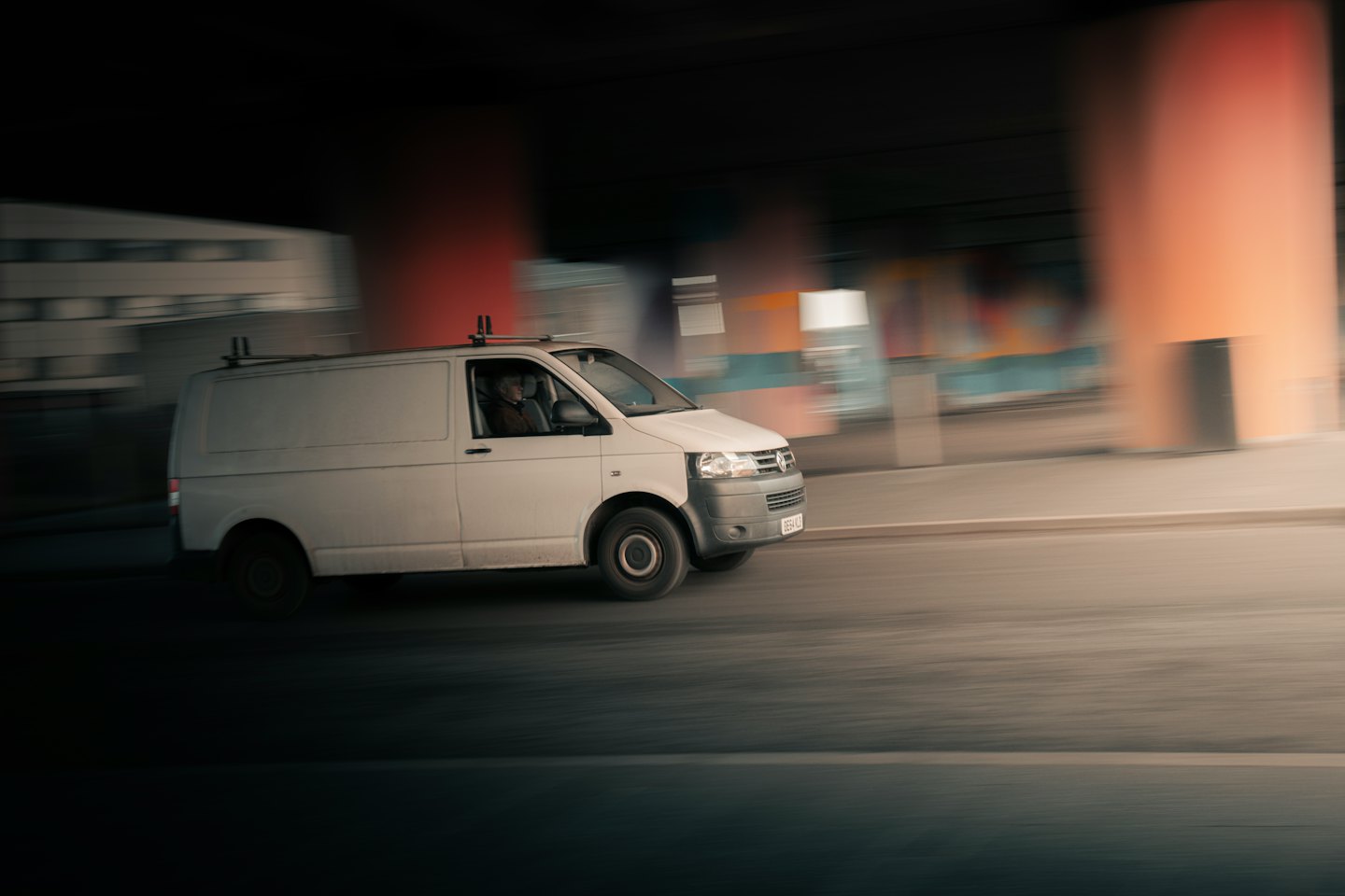 White cargo van drives quickly under a concrete overpass.